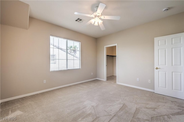 unfurnished bedroom with a walk in closet, baseboards, visible vents, and light colored carpet