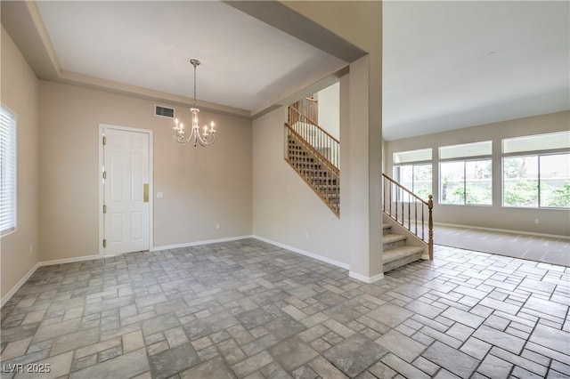 empty room featuring stone finish floor, visible vents, baseboards, a chandelier, and stairs