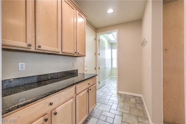 kitchen featuring dark stone counters, light brown cabinets, baseboards, and stone tile flooring