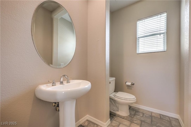 bathroom featuring toilet, stone tile flooring, and baseboards