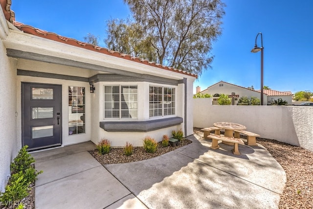 doorway to property with a tiled roof, a patio, stucco siding, and fence