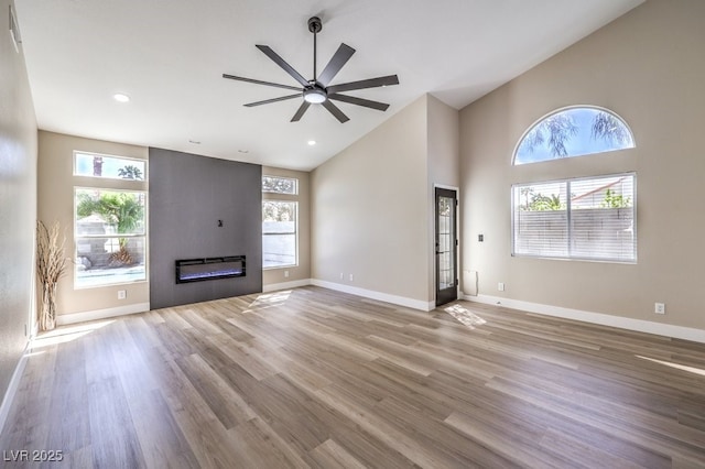 unfurnished living room featuring wood finished floors, a ceiling fan, baseboards, a fireplace, and high vaulted ceiling