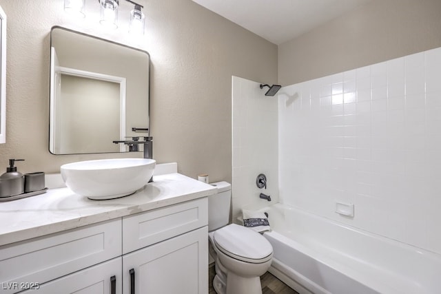 bathroom with washtub / shower combination, a textured wall, toilet, and vanity