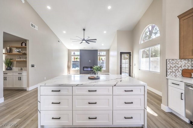 kitchen with visible vents, light wood-style floors, a center island, baseboards, and ceiling fan