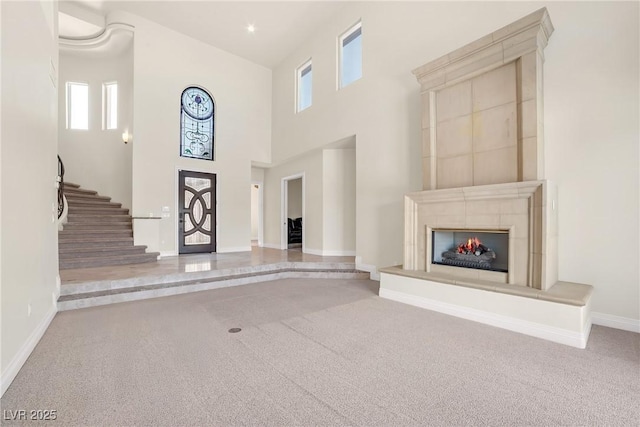 unfurnished living room featuring baseboards, a warm lit fireplace, carpet, and a towering ceiling