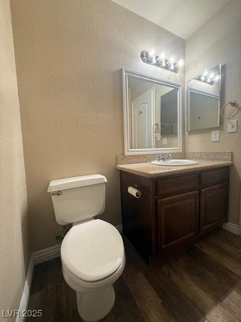 half bathroom with toilet, vanity, wood finished floors, and baseboards