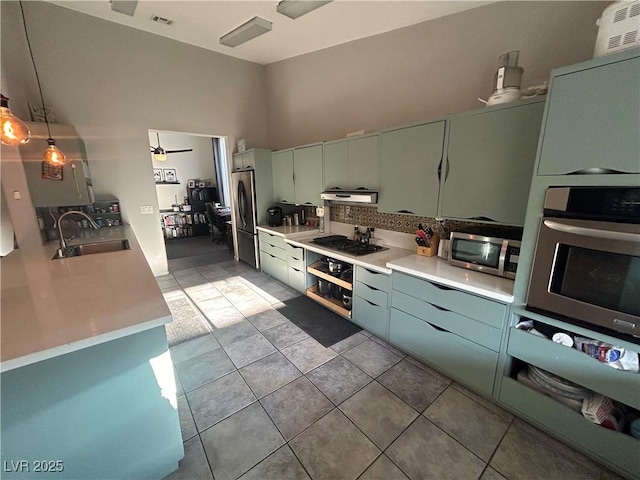 kitchen featuring a sink, stainless steel appliances, under cabinet range hood, light countertops, and a high ceiling