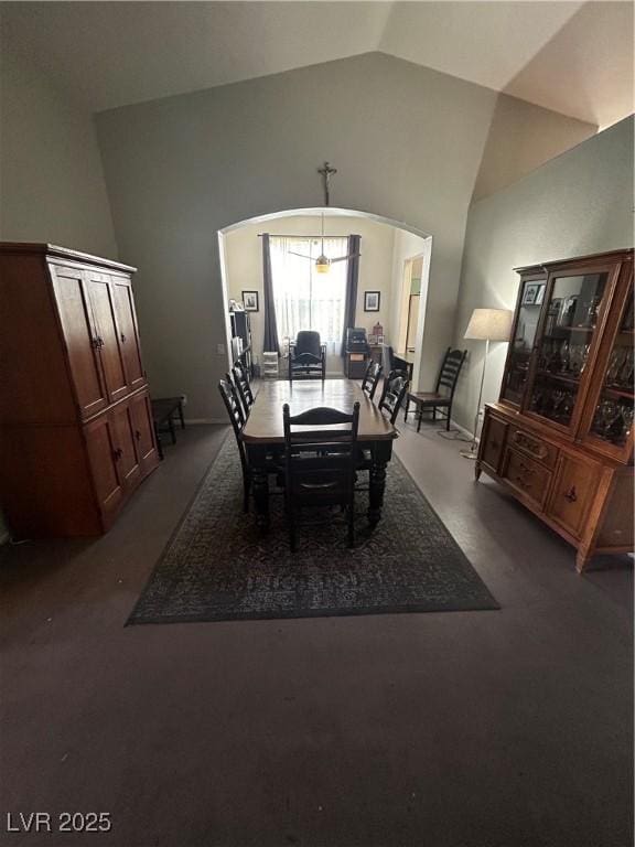dining area with arched walkways, dark carpet, baseboards, and high vaulted ceiling