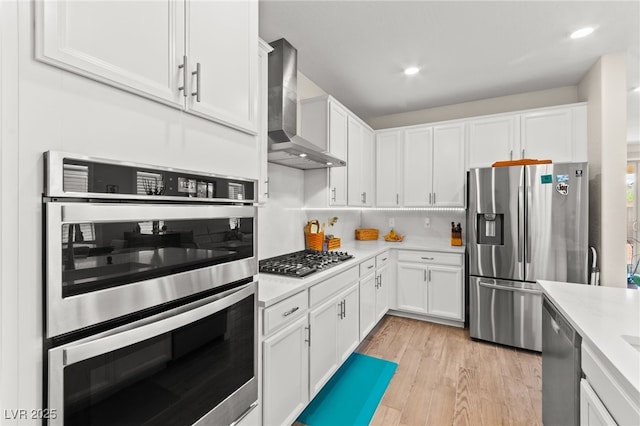 kitchen featuring light countertops, wall chimney range hood, appliances with stainless steel finishes, and white cabinetry