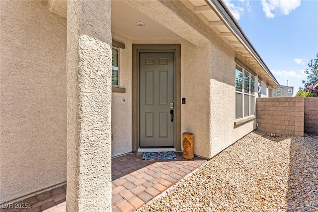 view of exterior entry featuring stucco siding and fence