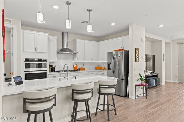 kitchen with a kitchen breakfast bar, visible vents, light wood-type flooring, wall chimney exhaust hood, and appliances with stainless steel finishes