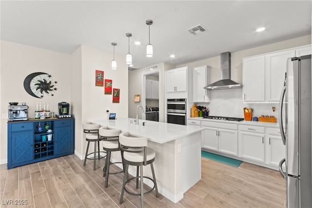 kitchen with a peninsula, wall chimney exhaust hood, stainless steel appliances, and light wood-style floors