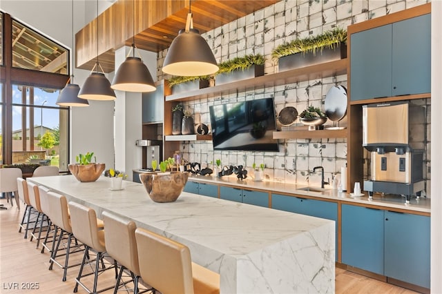 kitchen featuring open shelves, a sink, blue cabinets, a breakfast bar, and light wood-style flooring
