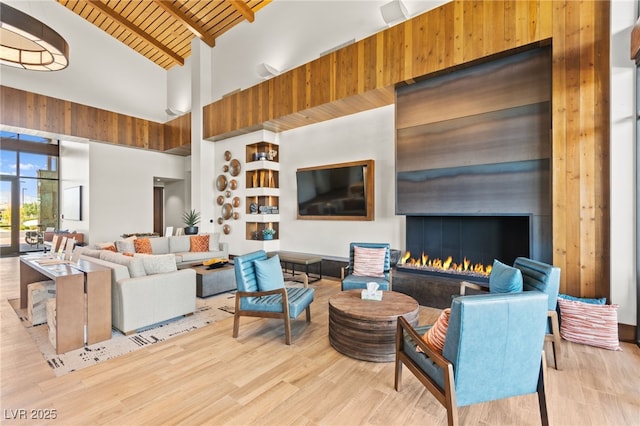 living room with high vaulted ceiling, a warm lit fireplace, beam ceiling, and wood finished floors