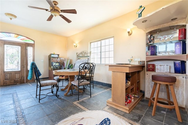 dining space featuring stone tile floors, ceiling fan, and baseboards