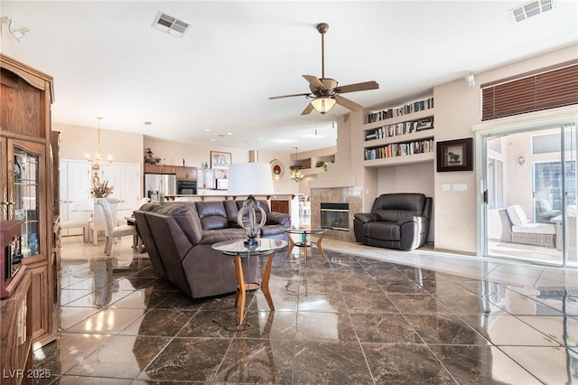living room featuring built in shelves, ceiling fan with notable chandelier, visible vents, and a glass covered fireplace