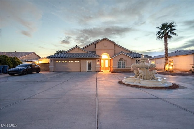 mediterranean / spanish-style house with stucco siding, driveway, a tiled roof, and a garage
