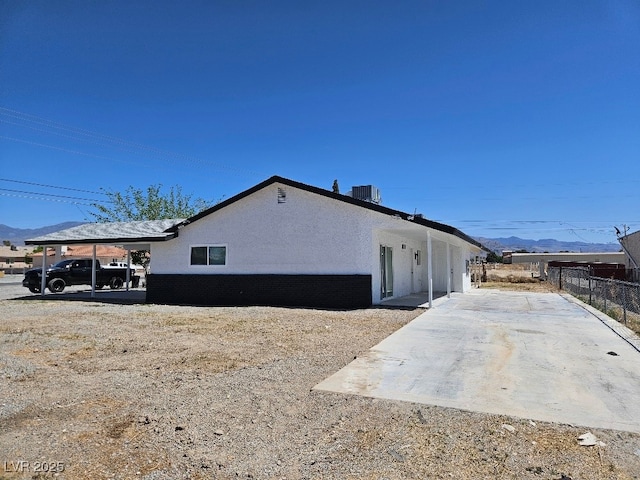 view of side of property featuring stucco siding, central AC unit, a mountain view, and fence