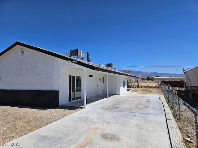 back of property featuring fence, stucco siding, a mountain view, central AC unit, and a patio