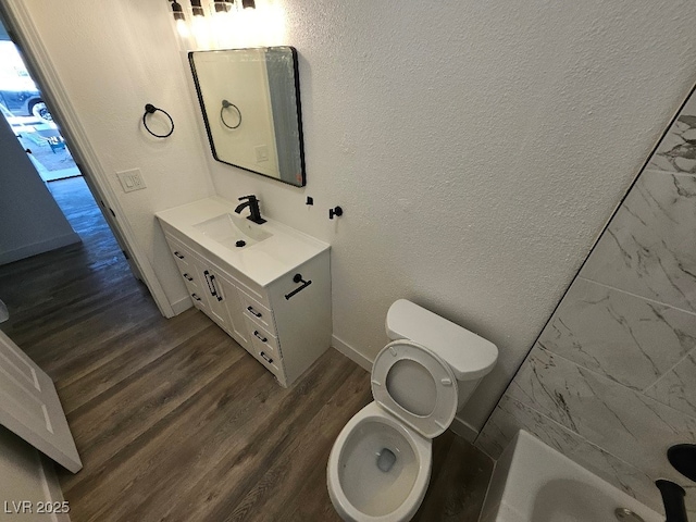 full bathroom with vanity, a textured wall, wood finished floors, toilet, and baseboards