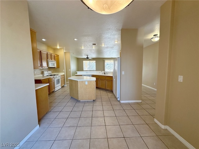 kitchen featuring a center island, a sink, light tile patterned flooring, white appliances, and light countertops