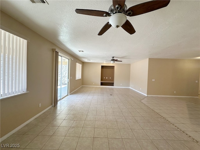 empty room with a textured ceiling, baseboards, ceiling fan, and light tile patterned floors