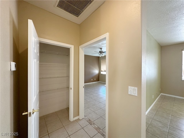 hall featuring baseboards, visible vents, a textured ceiling, and light tile patterned flooring