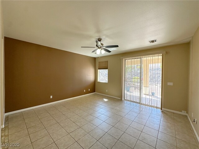 spare room featuring light tile patterned flooring, visible vents, a ceiling fan, and baseboards