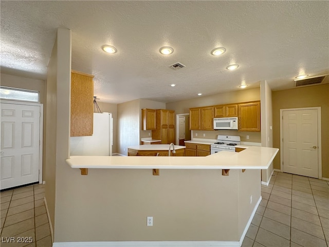 kitchen featuring light tile patterned floors, visible vents, white appliances, and a breakfast bar area