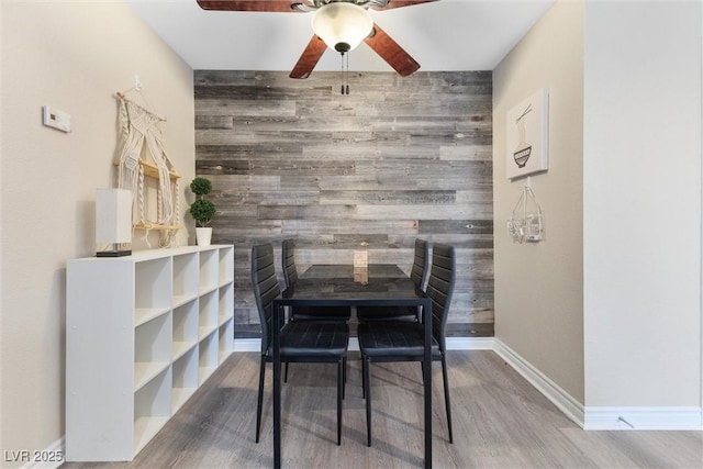 dining area featuring wooden walls, wood finished floors, baseboards, and ceiling fan