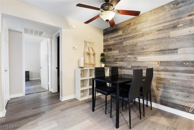 dining area with wooden walls, wood finished floors, visible vents, baseboards, and ceiling fan