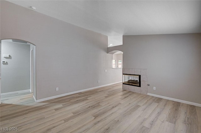 8028 Hurricane Cove Ct, Las Vegas, NV 89129 - unfurnished living room featuring light wood-type flooring, a tiled fireplace, baseboards, and arched walkways