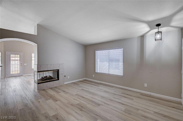 8028 Hurricane Cove Ct, Las Vegas, NV 89129 - unfurnished living room featuring light wood-style flooring, baseboards, arched walkways, and a tile fireplace