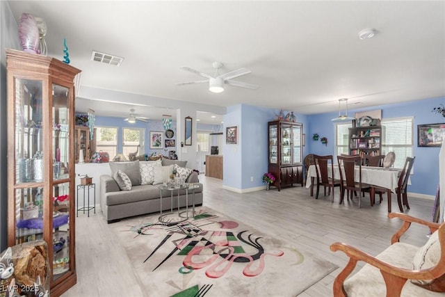 living room with baseboards, a ceiling fan, light wood-style floors, and visible vents