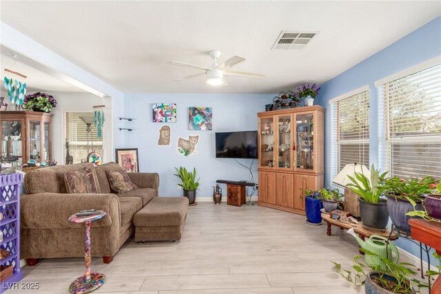 living area featuring visible vents, light wood finished floors, baseboards, and ceiling fan