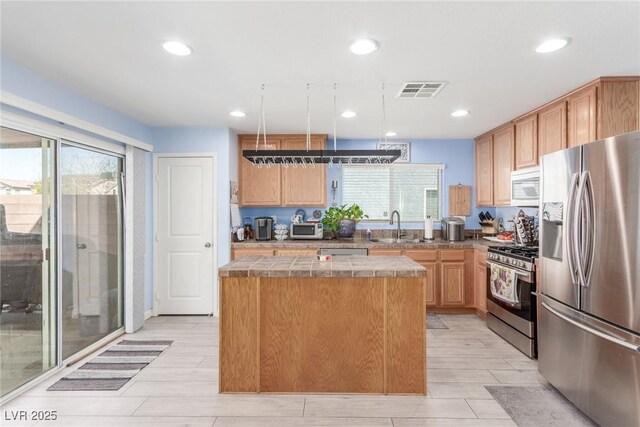 kitchen featuring stainless steel appliances, a sink, recessed lighting, tile counters, and a kitchen island