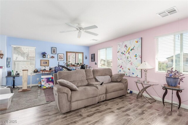 living area featuring baseboards, light wood-style flooring, visible vents, and ceiling fan