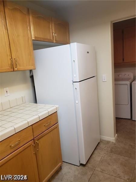 kitchen with washing machine and dryer, light tile patterned flooring, tile counters, and freestanding refrigerator