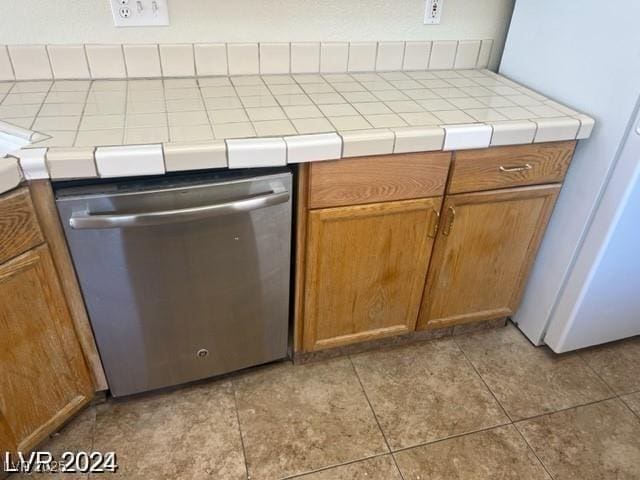 kitchen with brown cabinets, dishwasher, tile counters, and light tile patterned floors