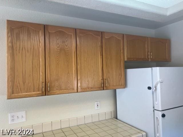 kitchen with tile countertops, brown cabinets, and freestanding refrigerator