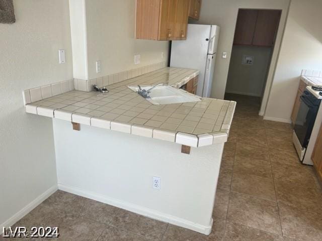 kitchen with a sink, freestanding refrigerator, baseboards, a peninsula, and range