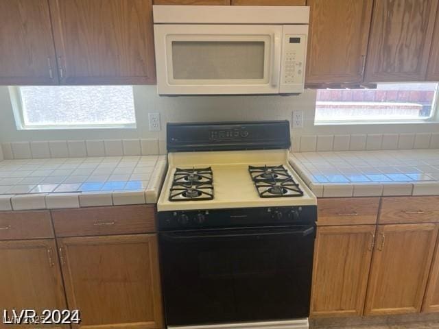 kitchen featuring gas range oven, tile countertops, plenty of natural light, and white microwave