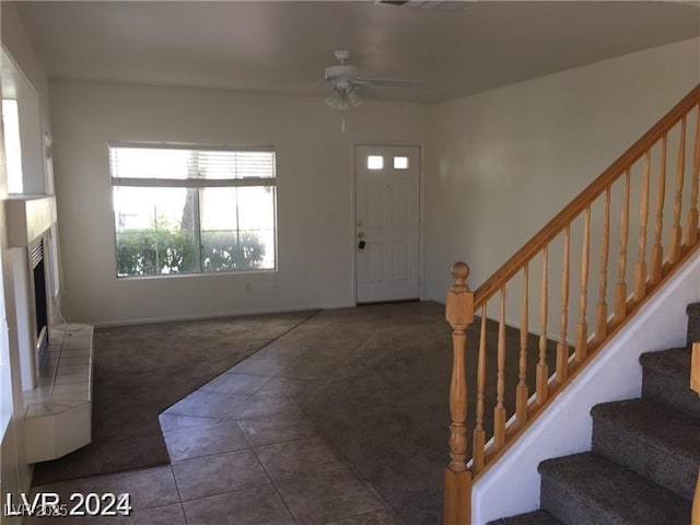 carpeted foyer featuring stairway, a fireplace with raised hearth, ceiling fan, baseboards, and tile patterned flooring