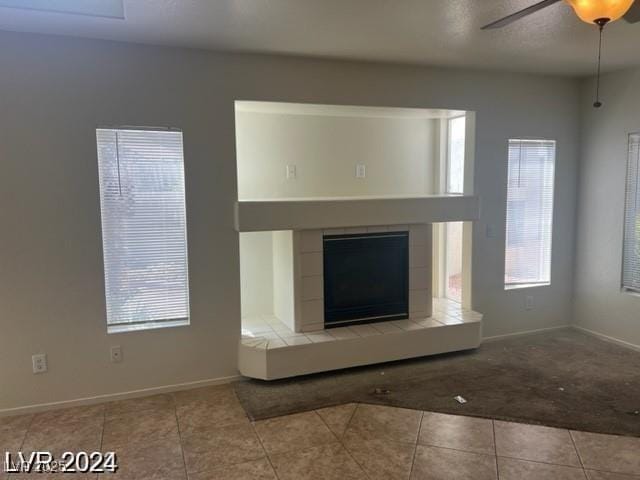 unfurnished living room featuring tile patterned floors, a tiled fireplace, baseboards, and a ceiling fan