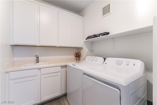 washroom featuring wood finished floors, a sink, separate washer and dryer, cabinet space, and visible vents
