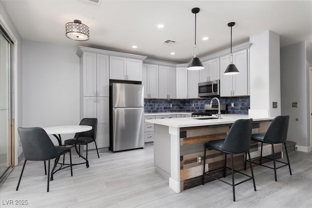 kitchen featuring stainless steel appliances, a peninsula, visible vents, light countertops, and a breakfast bar