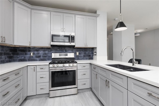 kitchen with stainless steel appliances, light countertops, gray cabinetry, and a sink