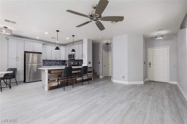 kitchen featuring stainless steel appliances, light countertops, a kitchen bar, backsplash, and visible vents