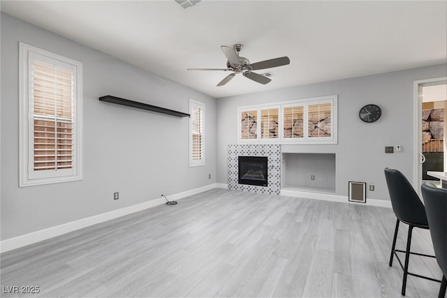 unfurnished living room featuring a fireplace, light wood-style floors, baseboards, and ceiling fan