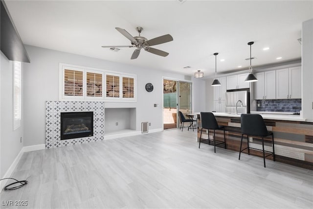 living area with a fireplace, light wood-style floors, baseboards, and ceiling fan